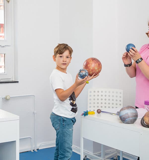 Schulkind hält Planetenmodelle in einer Smart-Einheit, daneben die Pädagogin